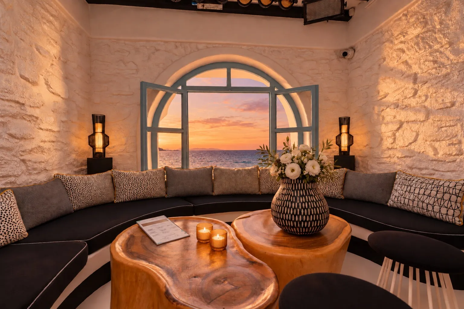 The Rotonda Table at BAO'S at sunset, the arched window open to an orange sky over the sea, candles on the amber wood tables