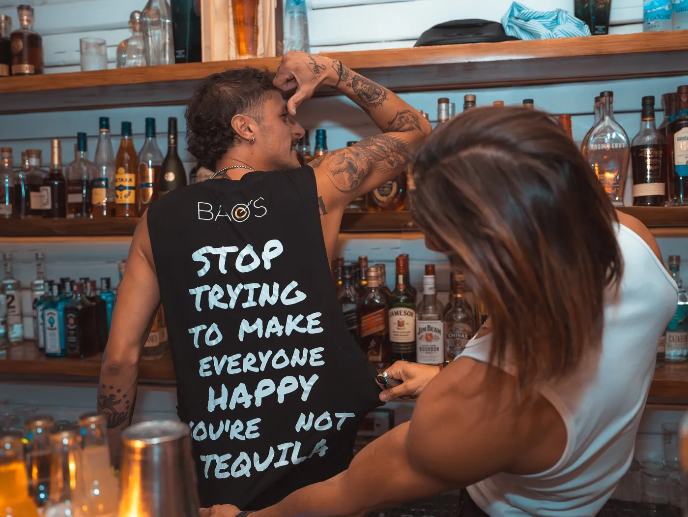 A bartender at BAO'S reaching up to the bottle shelf beside the bar's own sign