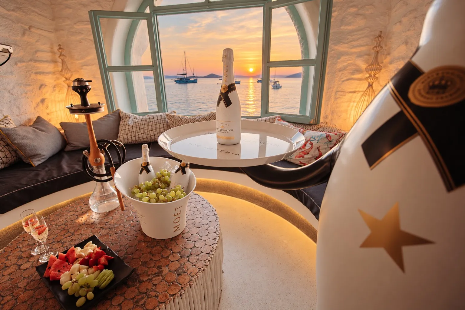 A shisha, a champagne bottle on ice and a fruit plate on the round table at BAO'S, sunset in the window behind