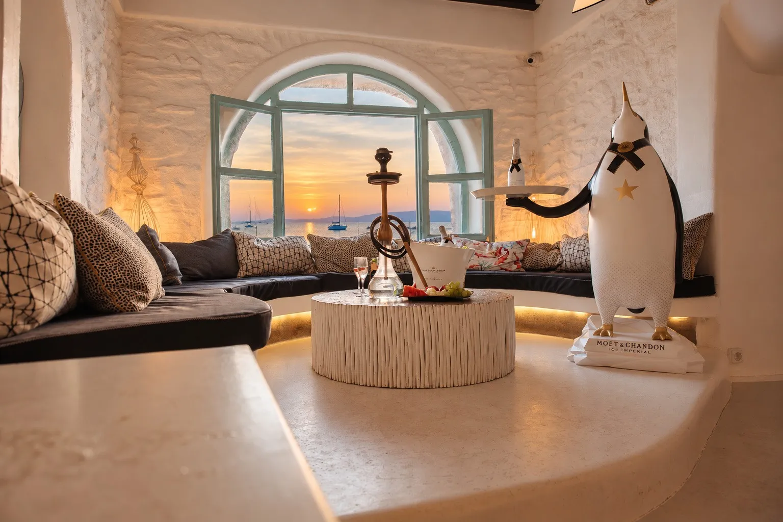 The shisha alcove at BAO'S in sunset light, cushions along the curved bench and the window open to the sea