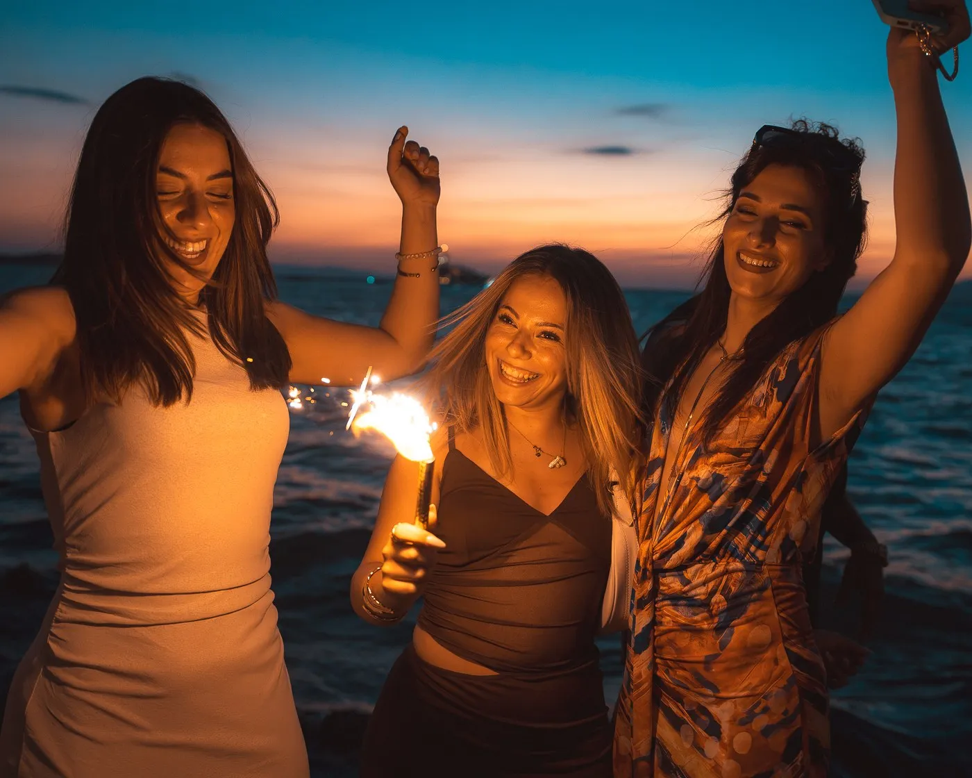 Three guests holding sparklers at the water's edge at BAO'S as the sun goes down