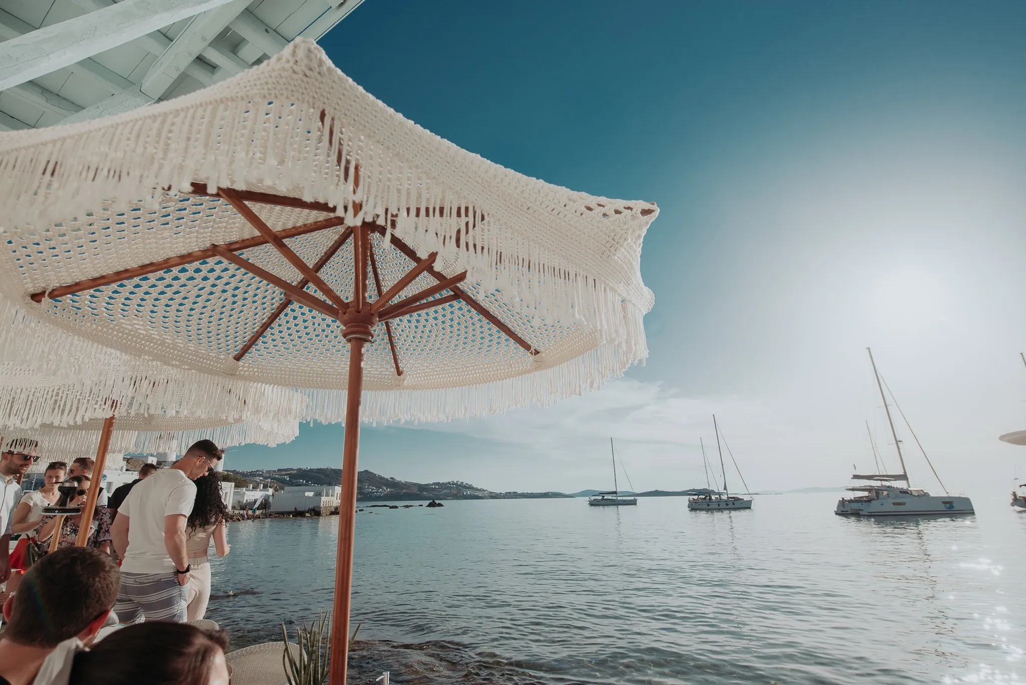 Makramee-Schirme über den Tischen am Meer im BAO'S, mit Booten in der Bucht dahinter