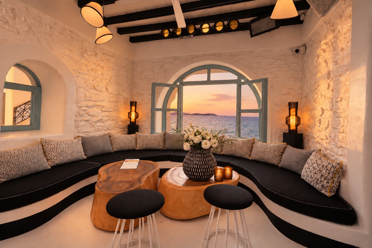 The Rotonda Table at sunset, lamps and candles lit, warm light across the cushions and the sun low in the arched window